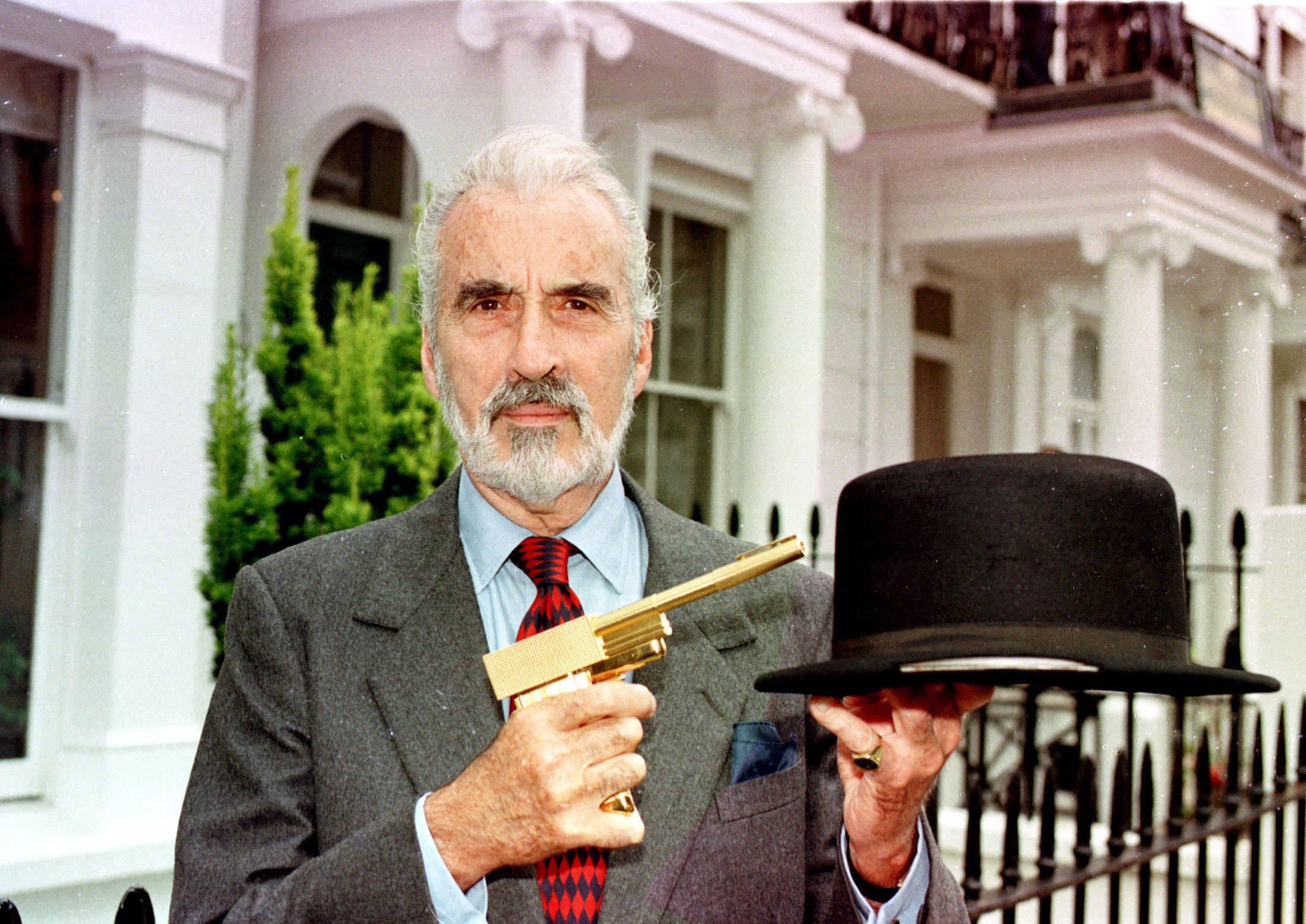 El siempre elegante y gran actor Christopher Lee, quien aparte de ejercer como Drácula interpretó con maestría al villano Scaramanga en ‘El hombre de la pistola de oro’ (1974). En la imagen, Lee posa en Londres en julio de 1998 junto con la mítica pistola de oro del filme y otro icono de la saga Bond, el sombrero con cuchila incorporada (varias décadas antes de ‘Peaky Blinders’) que usó Oddjob en ‘007 contra Goldfinger’ (1964). // MICHAEL STEPHENS
